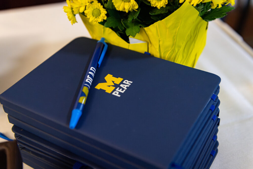 Notebook and pen with PEAR logo next to flowers.